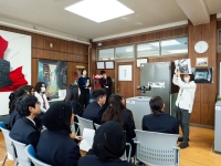 写真の左手に制服を着た生徒が背を向けて座り、右手にいる講師の方を向いている。講師は作家が彫刻作品を作っている写真を見せている。