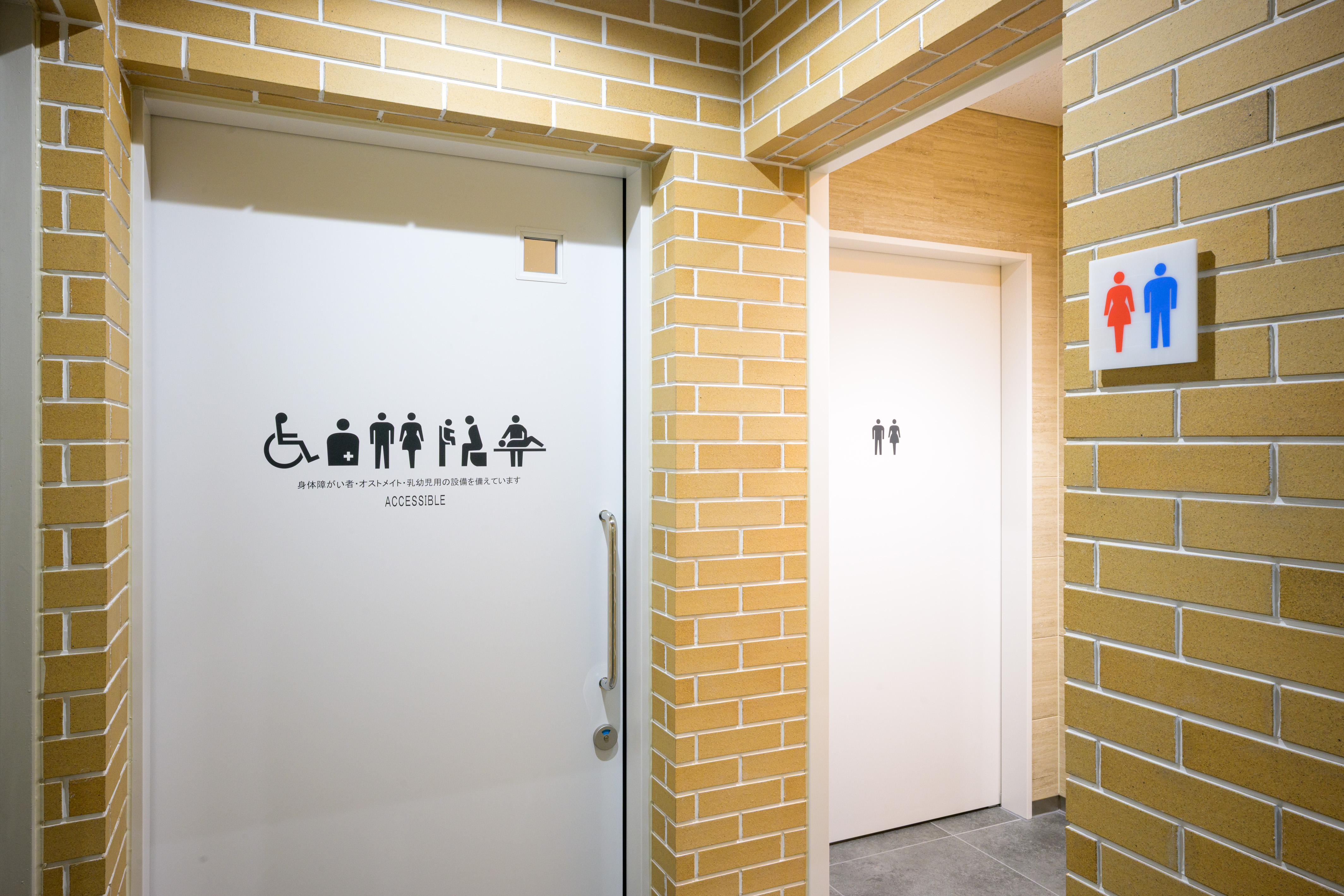 美術情報室前に2025年に増設した多機能トイレ入口。ドアにオストメイト対応、ユニバーサルシート設置のピクトグラム等を掲示。
