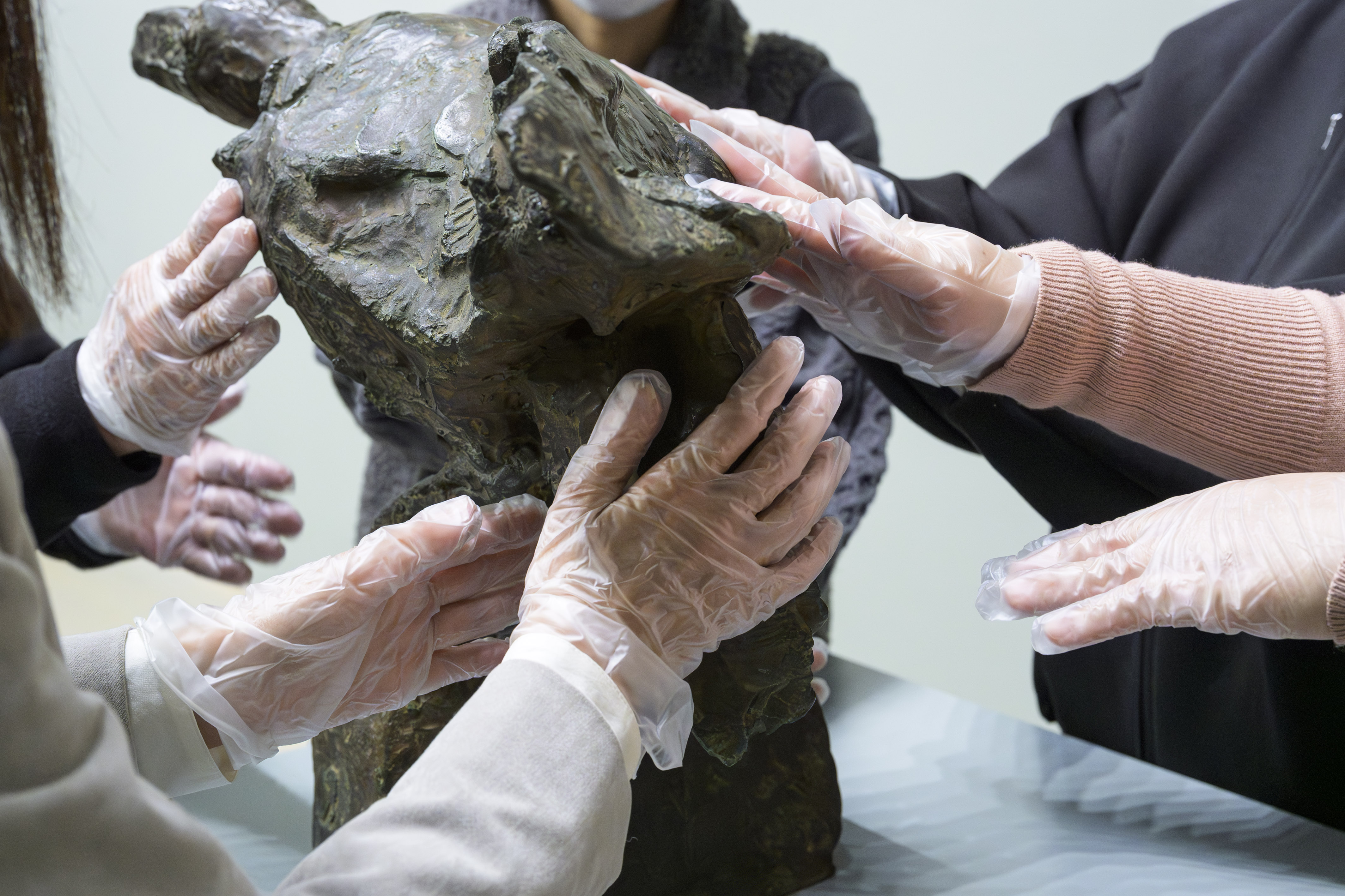 鳥をかたどったブロンズ彫刻の触察風景。参加者が手袋をつけて彫刻をさわる。