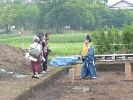 平安時代の衣装を着て建物跡を説明しています。